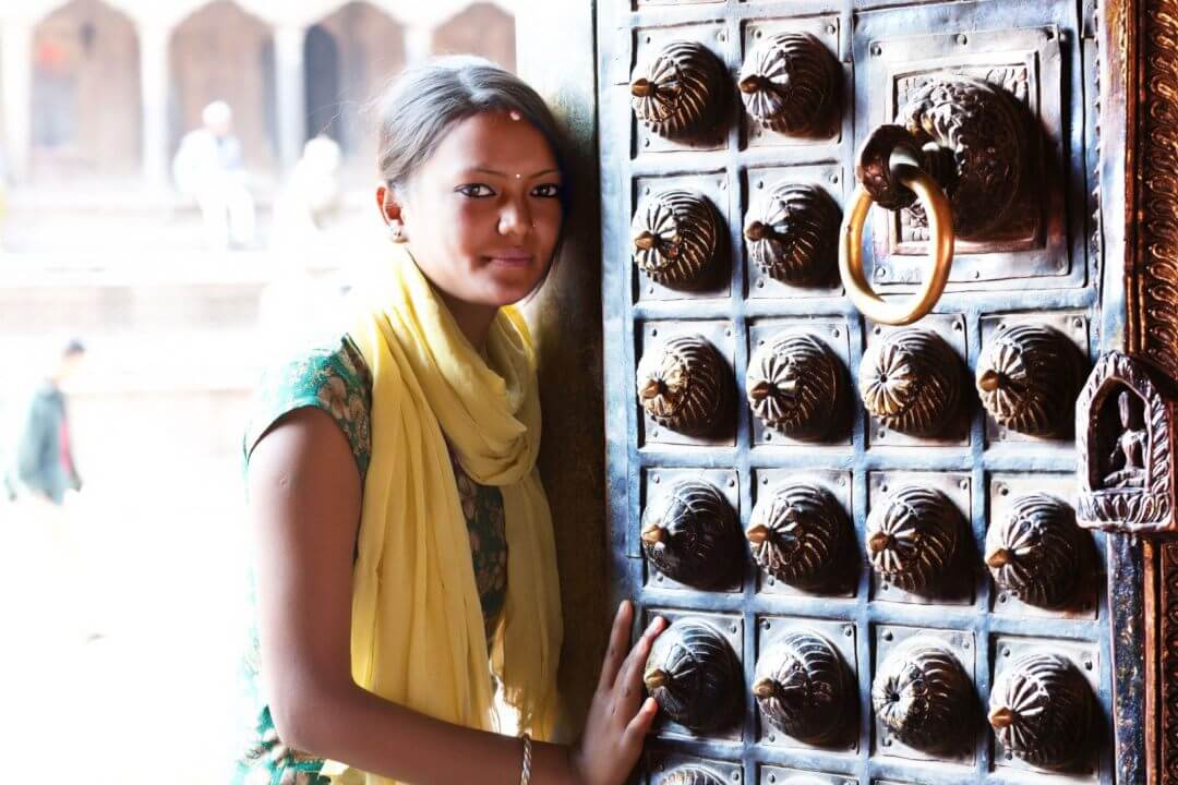 Femme n�palaise devant une porte traditionnelle sculpt�e, symbolisant l’artisanat authentique de Fleur du N�pal